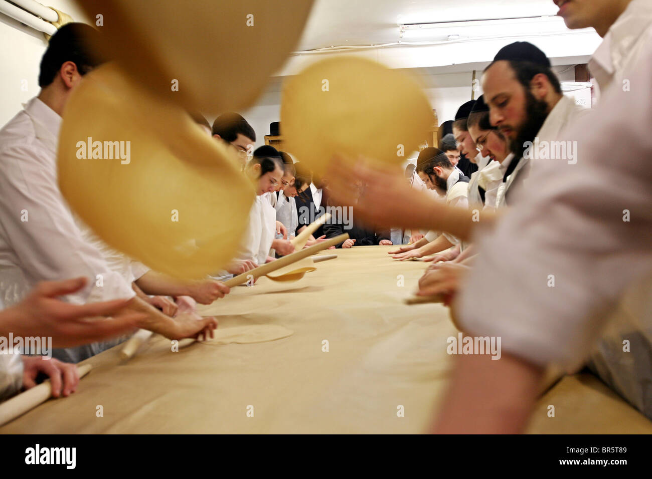 Teams of Orthodox Jewish teenage boys use rolling pins to flatten the matza bread for Passover before it goes into the oven. Stock Photo