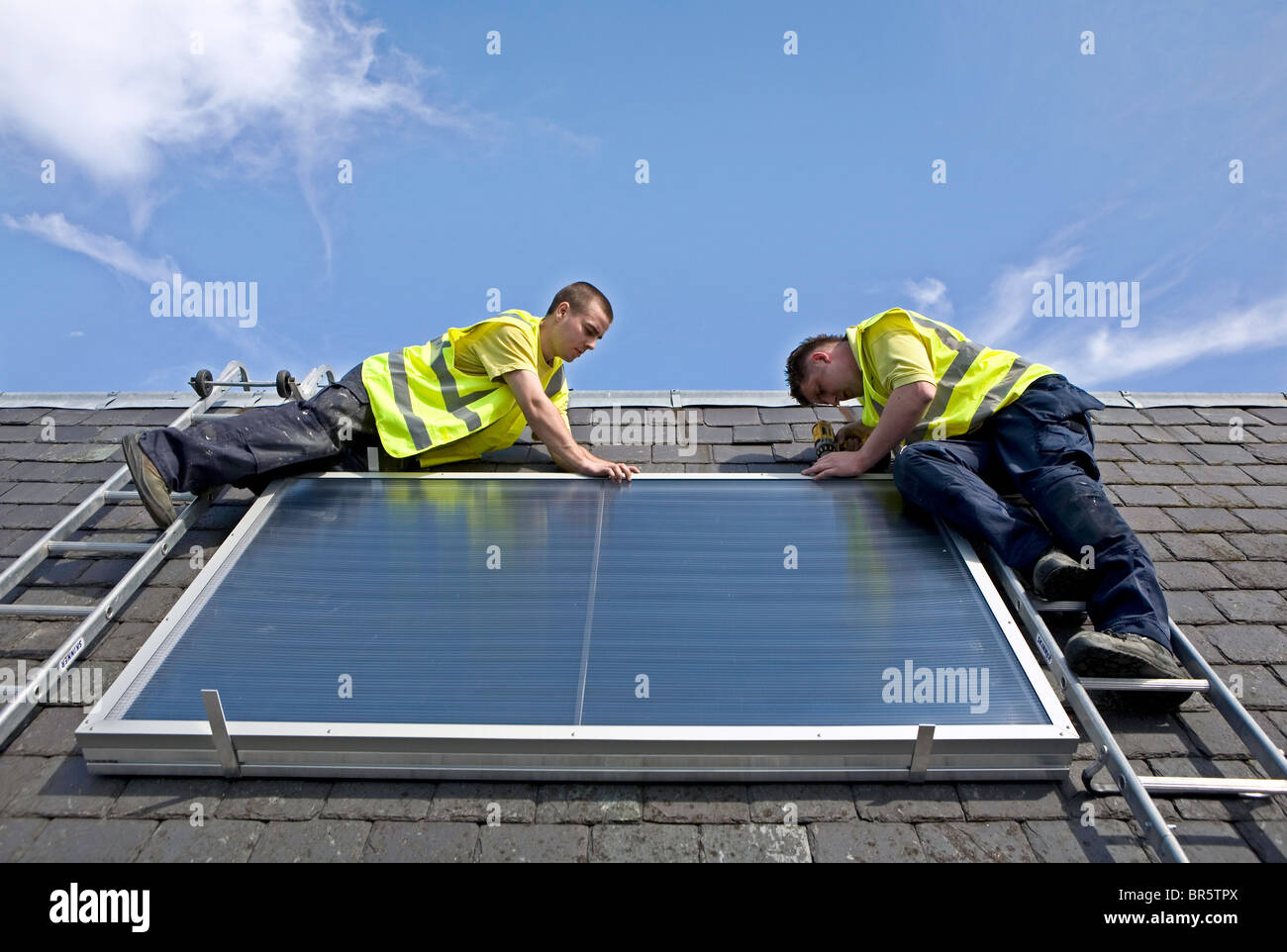 Workmen installing a solar thermal panel on a rooftop. Stock Photo