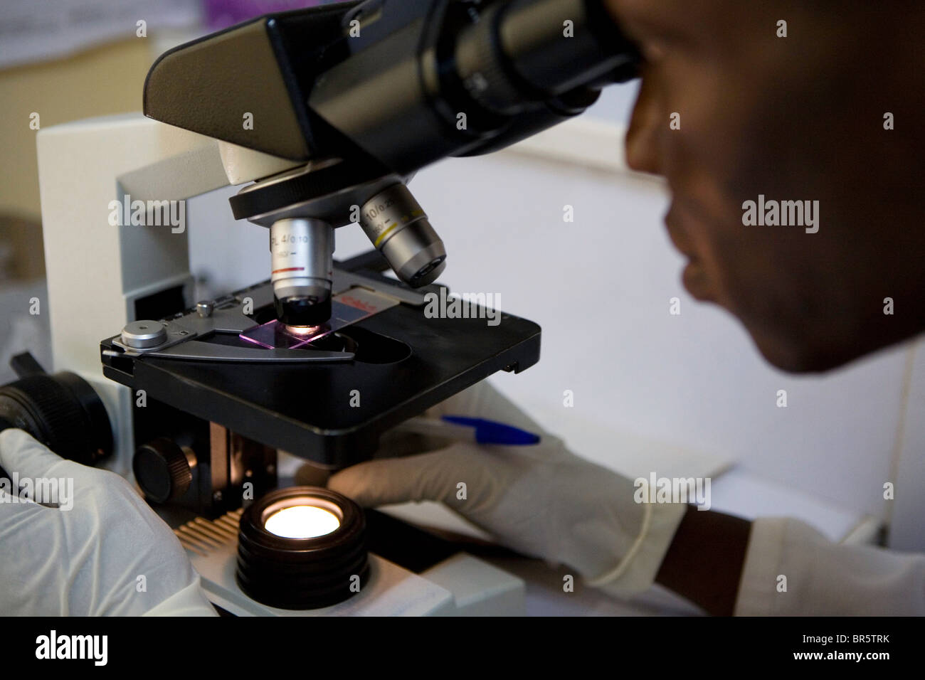 Laboratory technician looks through a microscope, searching through samples of blood for Malaria. Afrikids Medical Centre, Ghana Stock Photo