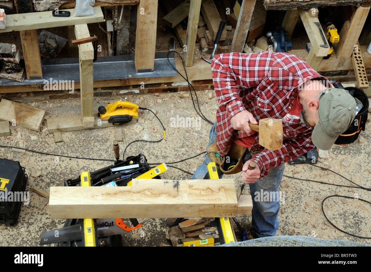 Renovating an old timber framed building carpenter using a chisel to form a joint on green oak timber Stock Photo