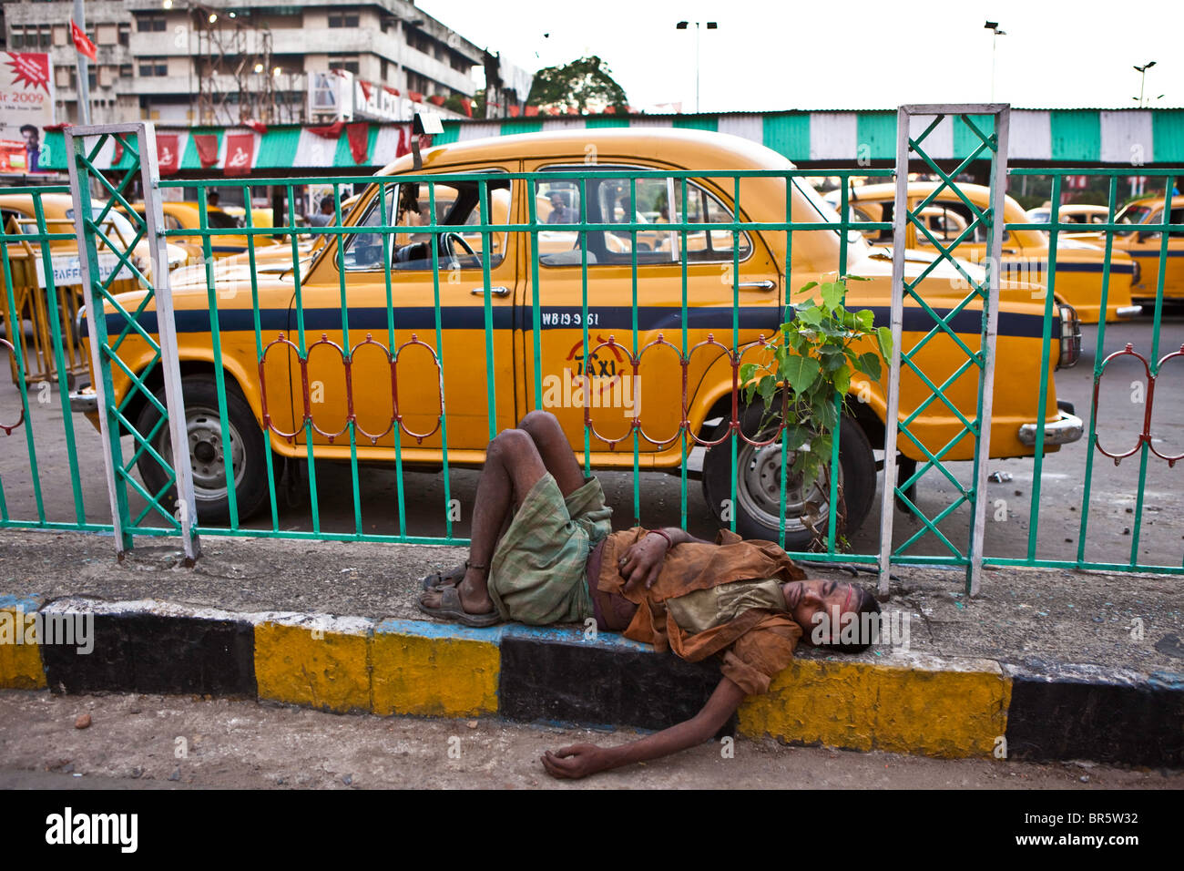 A homeless man lies asleep on the pavement outside the busy Kolkata train station. Stock Photo
