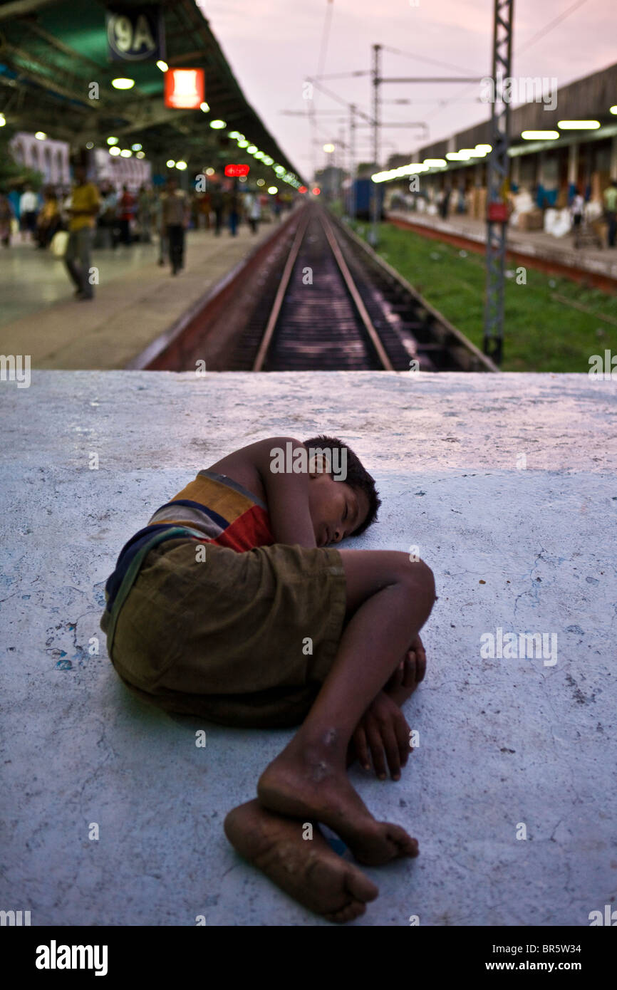 A young homeless boy sleeps on train buffers in the busy Kolkata train station. Stock Photo