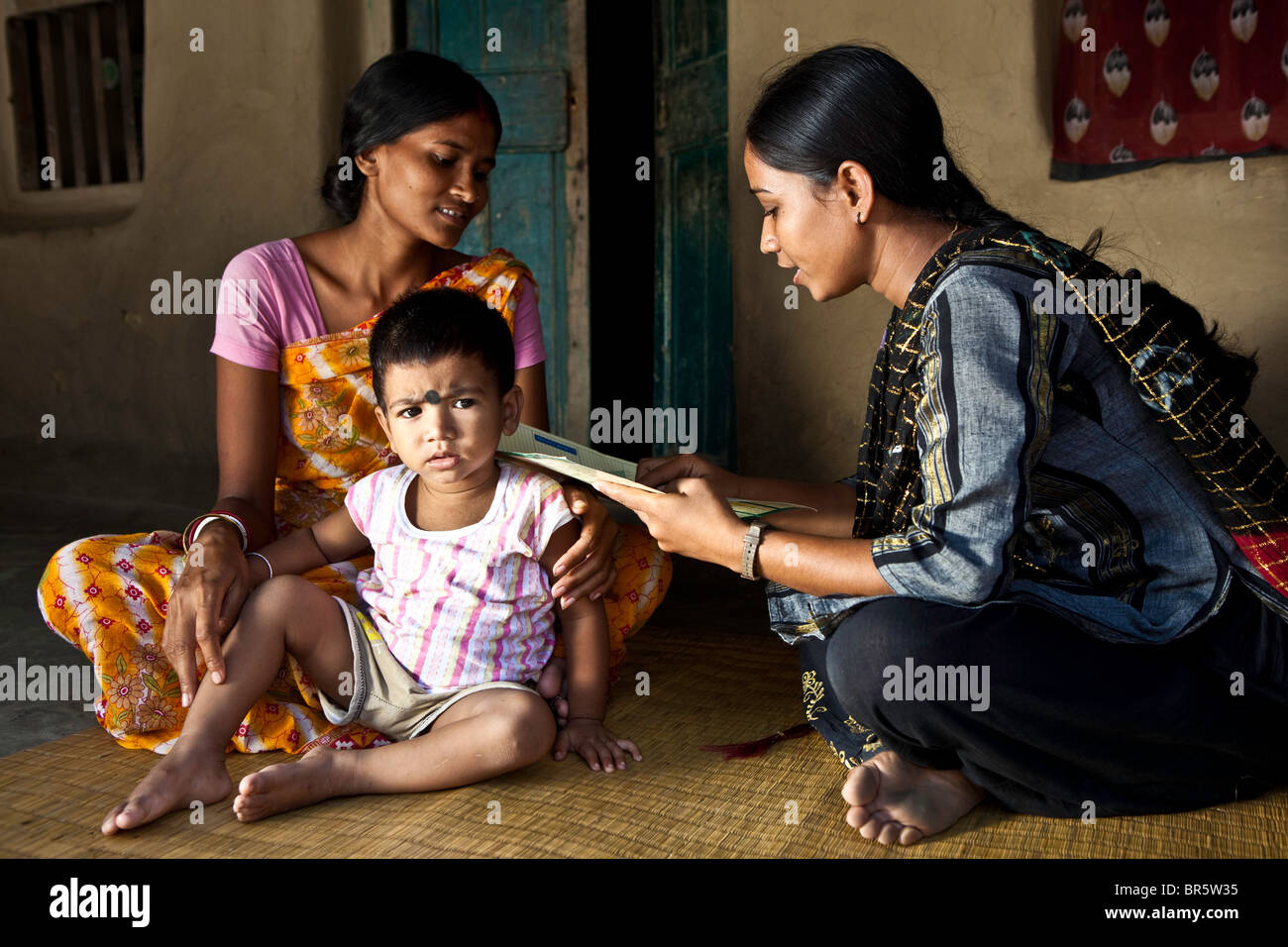 A female health worker makes a home visit to check on the progress of a mother and her daughter. Stock Photo