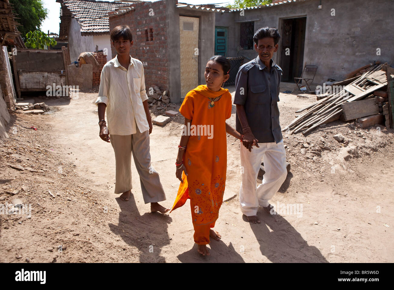 Hansa who is deaf and blind walks through her village accompanied by her father and brother. Stock Photo