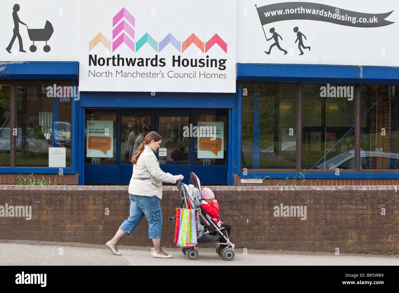 A woman pushing a child in a pram walks past the office door of Northwards housing. Stock Photo