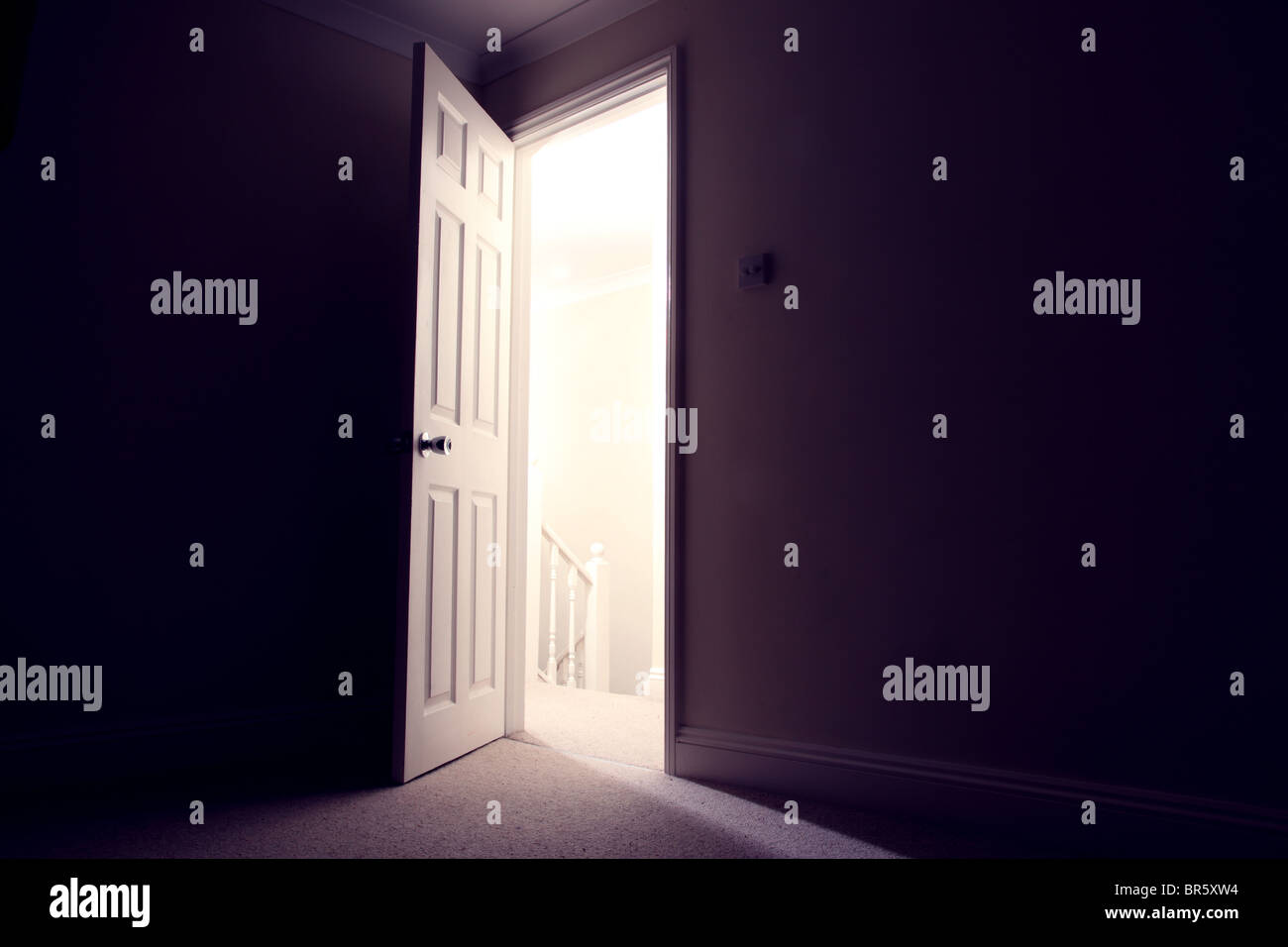 Dark room with open door light streaming in Stock Photo