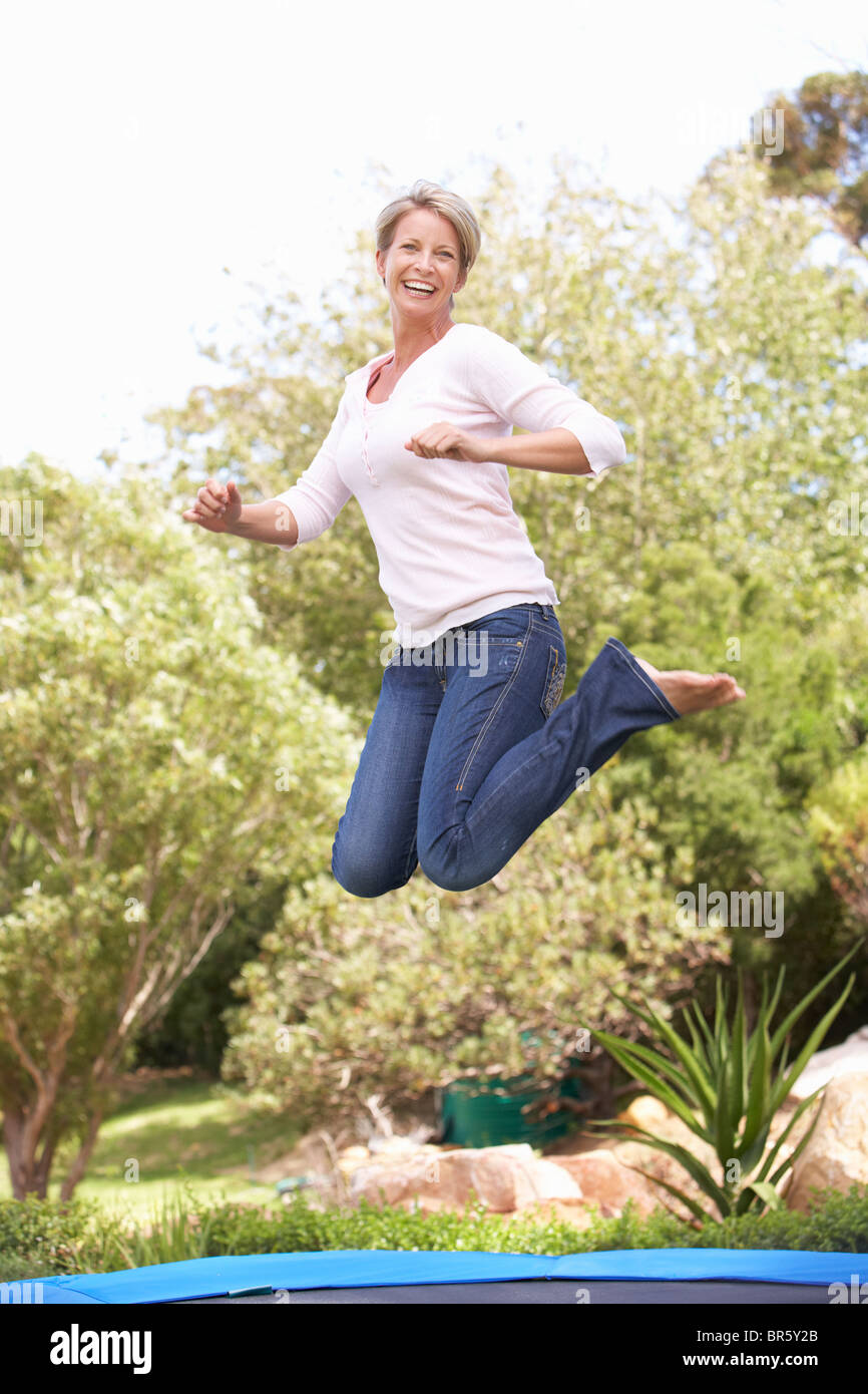 Woman Jumping On Trampoline In Garden Stock Photo