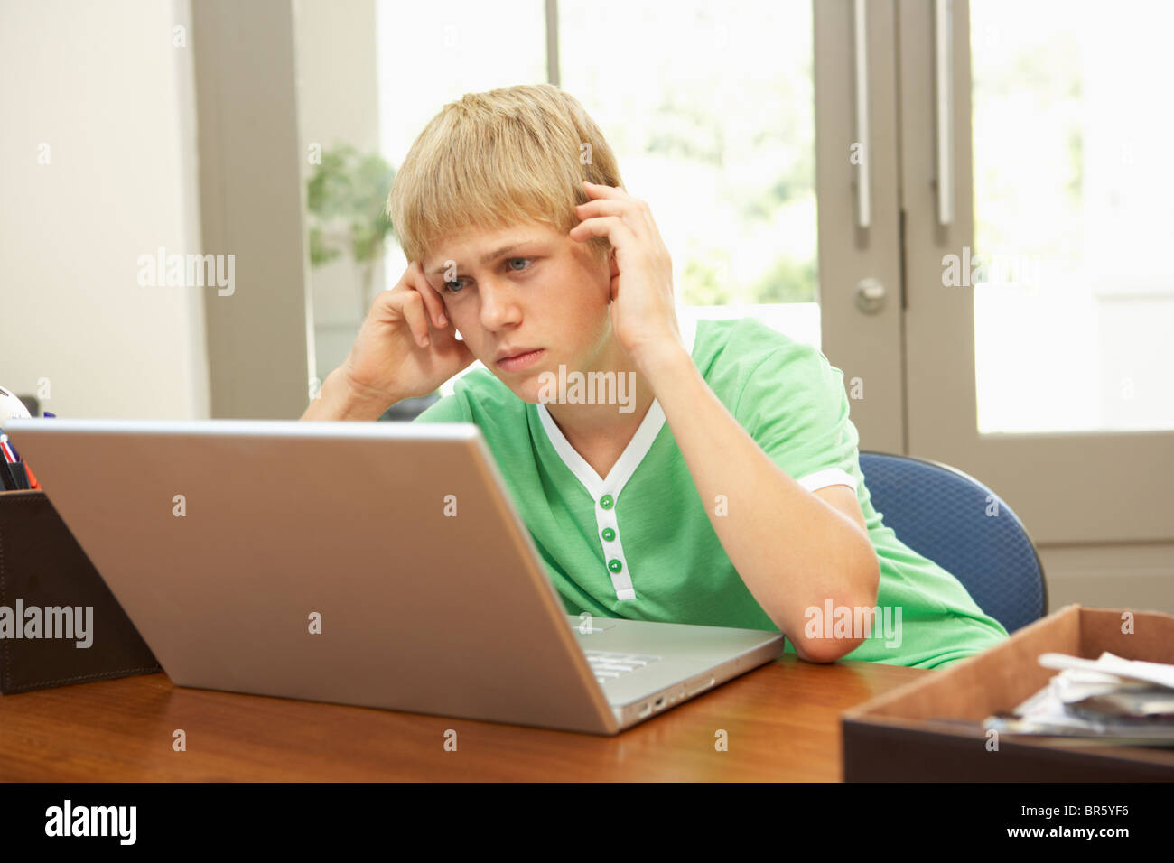 Worried Looking Teenage Boy Using Laptop At Home Stock Photo