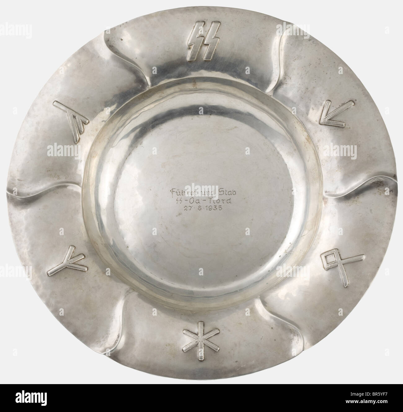 A silver rune-decorated dish, honour gift by SS-Gruppenführer Werner Lorenz Hand-hammered silver with mark of fineness '800 handgehämmert' (hand-hammered) on the bottom. The border displays a series of runes (Sig, Tyr, Odal, Algiz/life rune) in high relief. In the centre the engraved dedication 'Führer und Stab - SS Oa Nord - 27.8.1935' (Commander and Staff - SS Oa North - 27 August 1935). Werner Lorenz (1891 - 1974) was assigned as Commander, SS-Oberabschnitt Nord (northern superior district) from February 1934 to March 1937 with his office located in Hamburg., Stock Photo