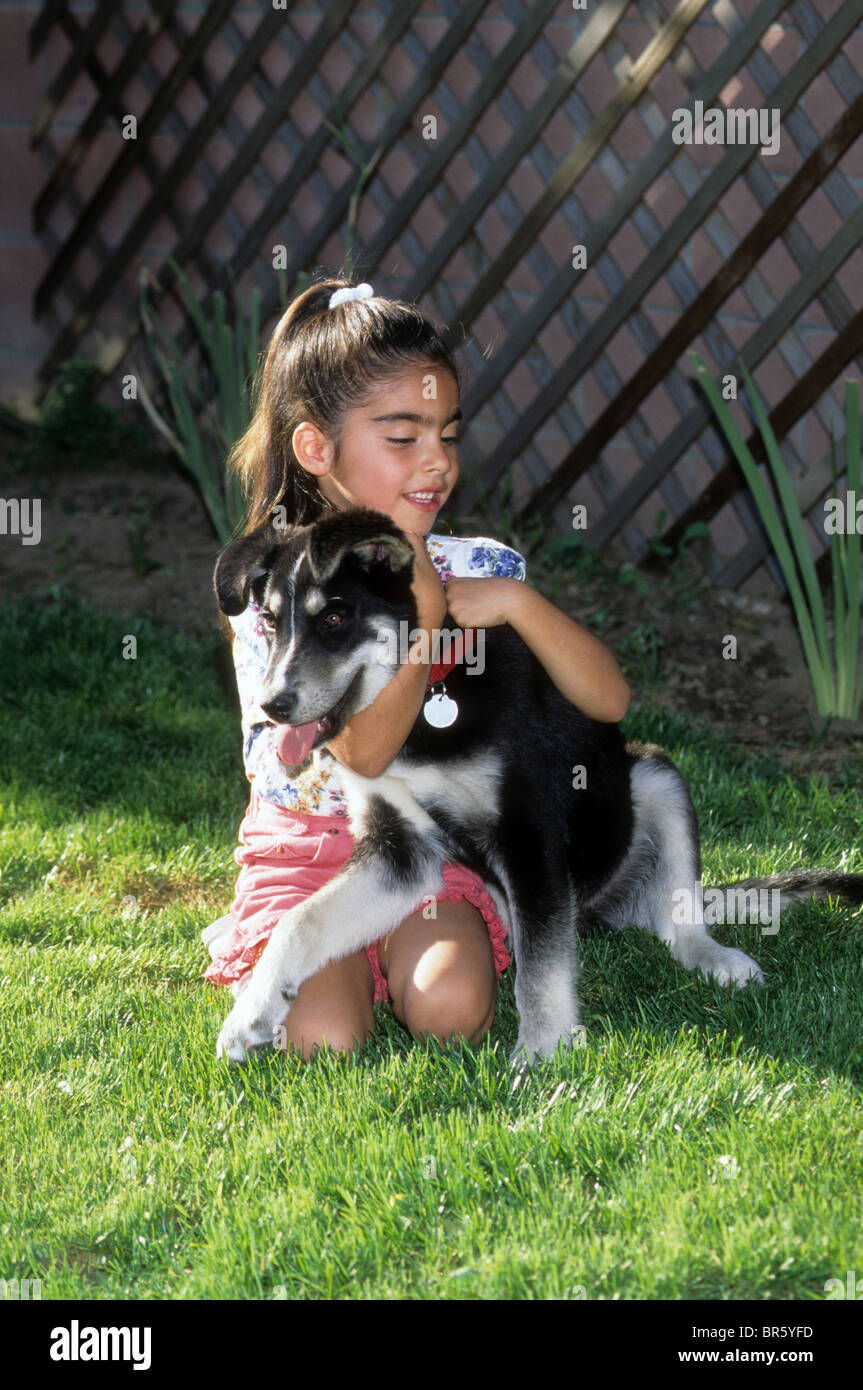 Young Hispanic girl hugs pet puppy dog love smile happy eager care Stock Photo