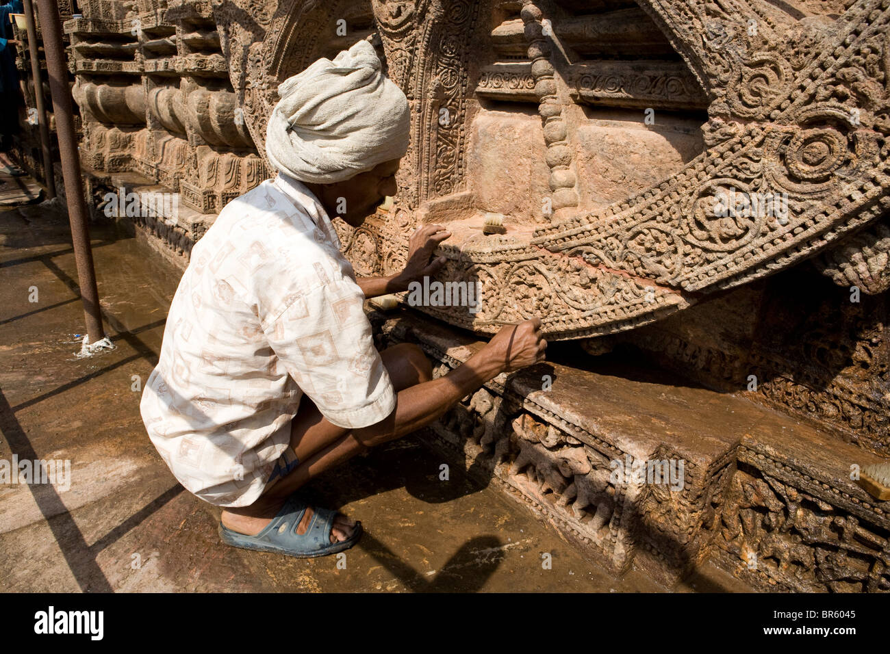 An Indian man is cleaning by a small brush part of the old wheel at Sun Temple in Konark, Orissa, India. Stock Photo