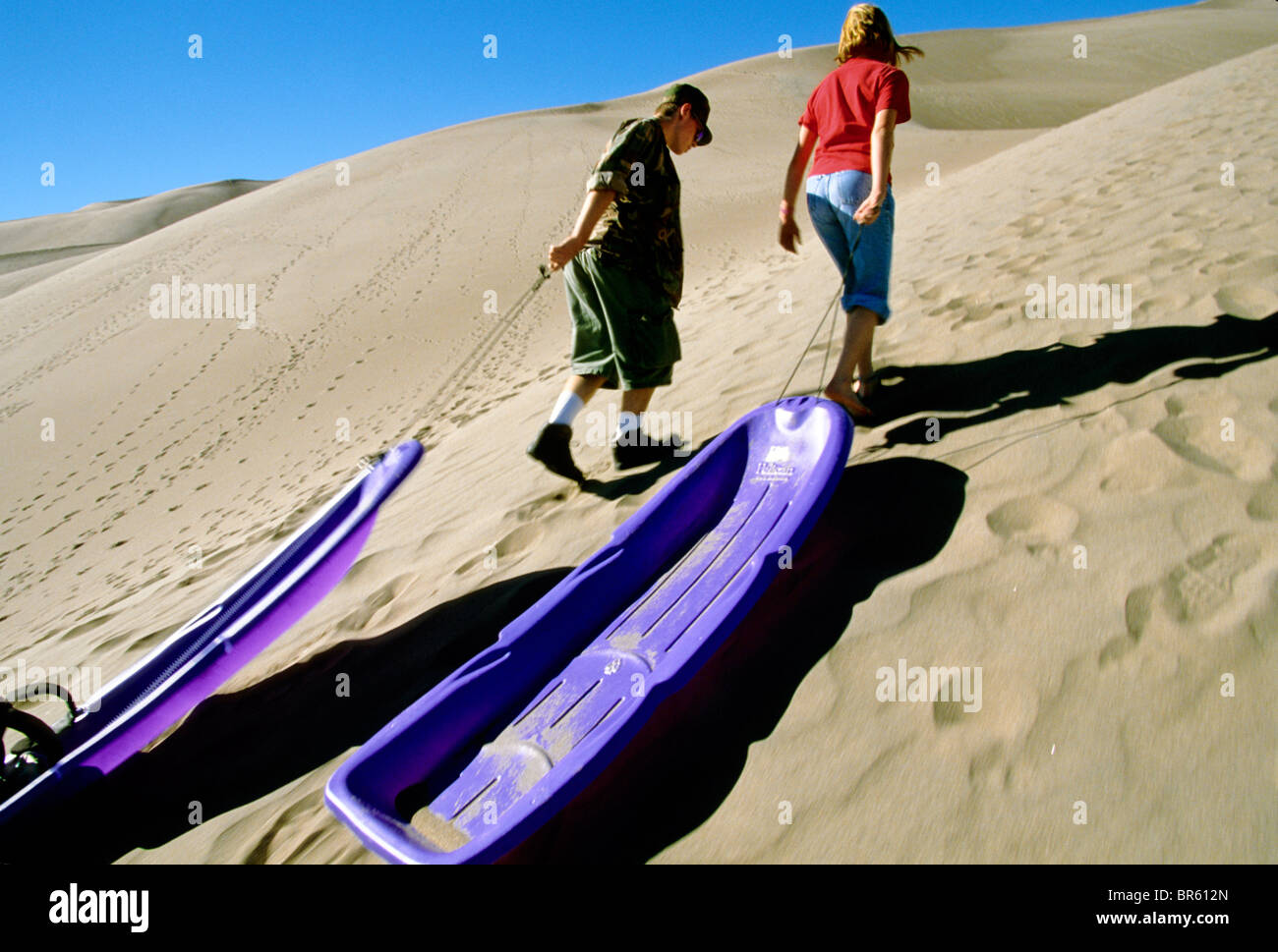 Two kids carry their sleds on top of a sand dune in Great Sand Dunes