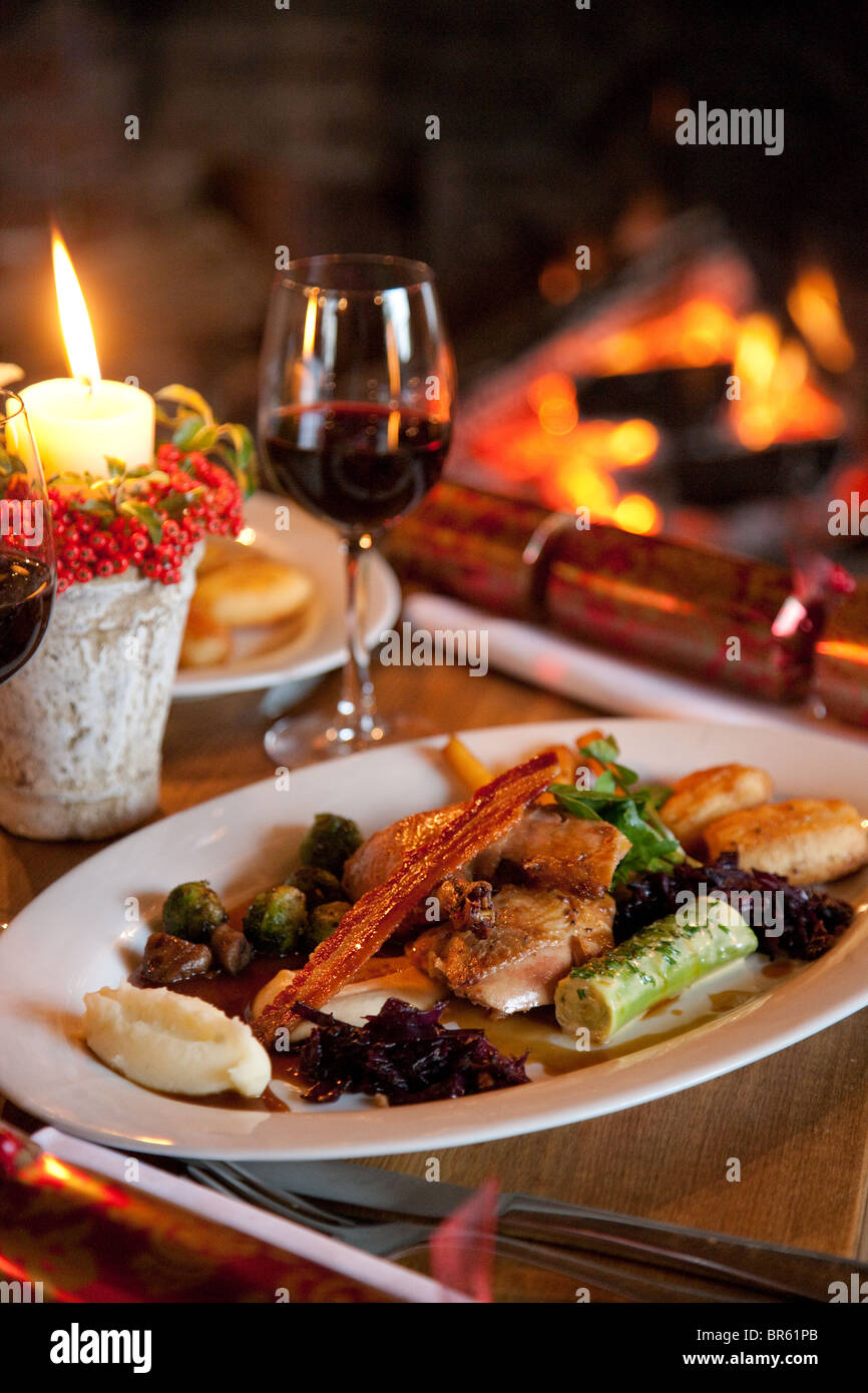 Christmas dinner and pudding on a plate by the roaring fireplace with decorations Stock Photo