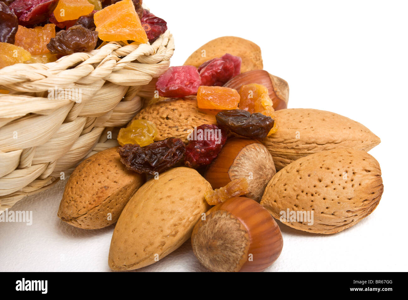 Mixed dried fruits and nuts spilling from basket on white background. Stock Photo
