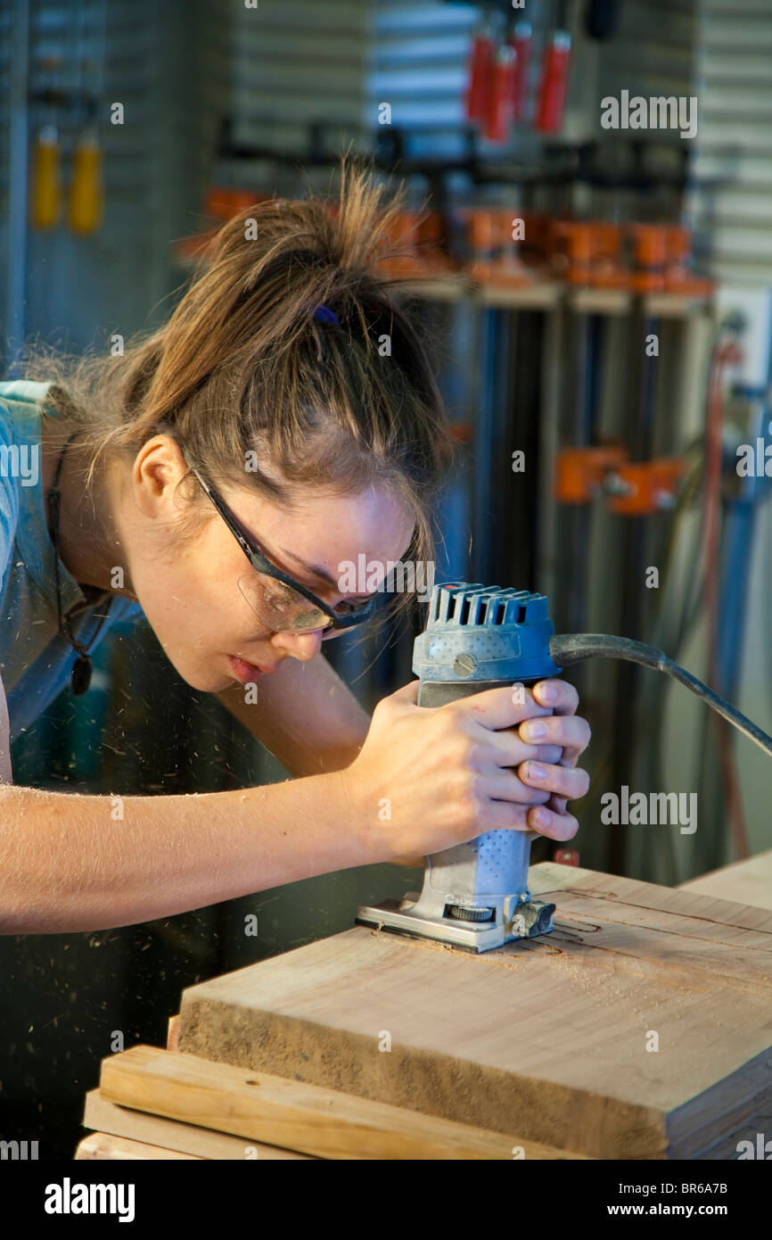 Young female apprentice sanding a cabinet part in a woodshop. Stock Photo