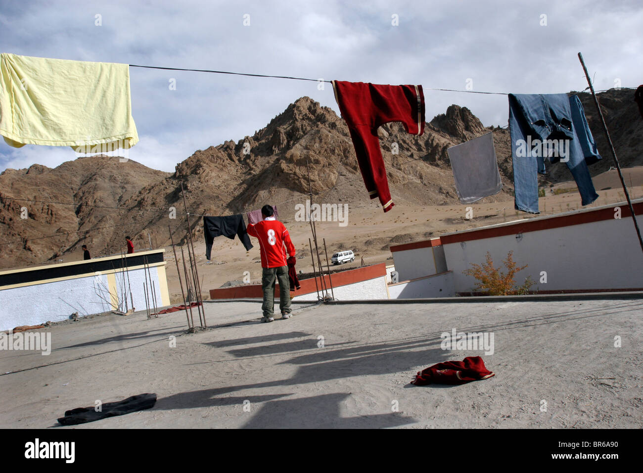 A boy hangs laundry to dry on the roof of a boys' school at a Buddhist monastery in the outskirts of Leh in Ladakh, India. Stock Photo