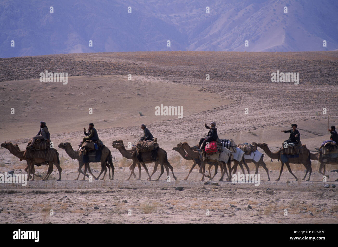 Men ride camels through the barren hills of the Samangan region Stock Photo