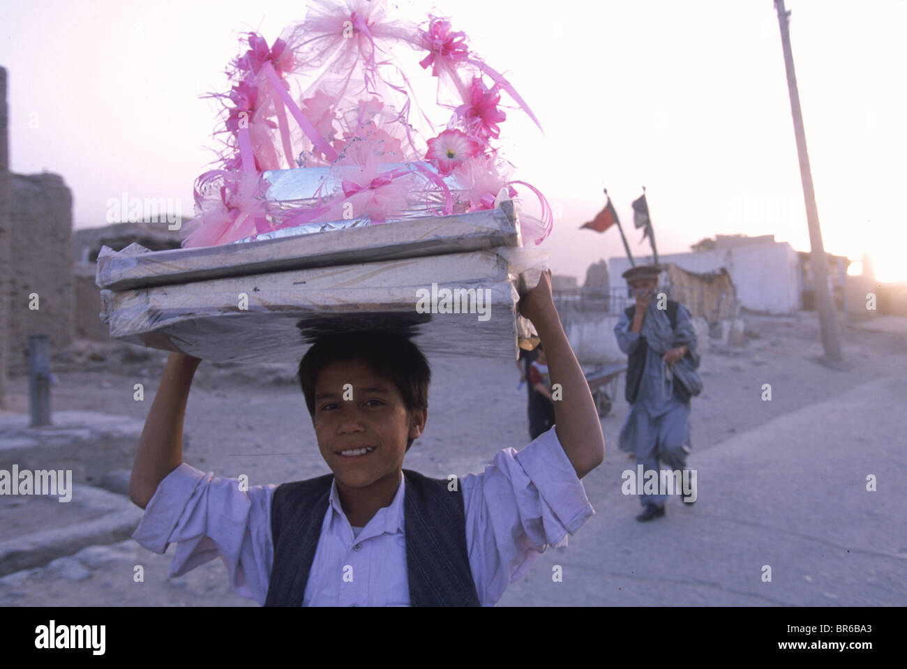 A boy carries a frilly pink ornament for the top of a wedding cake through the dusty streets of old Kabul Afghanistan Stock Photo