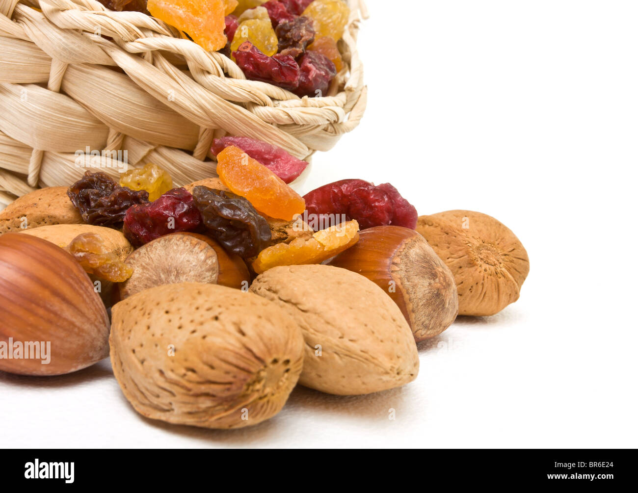 Mixed dried fruits and nuts spilling from basket on white background