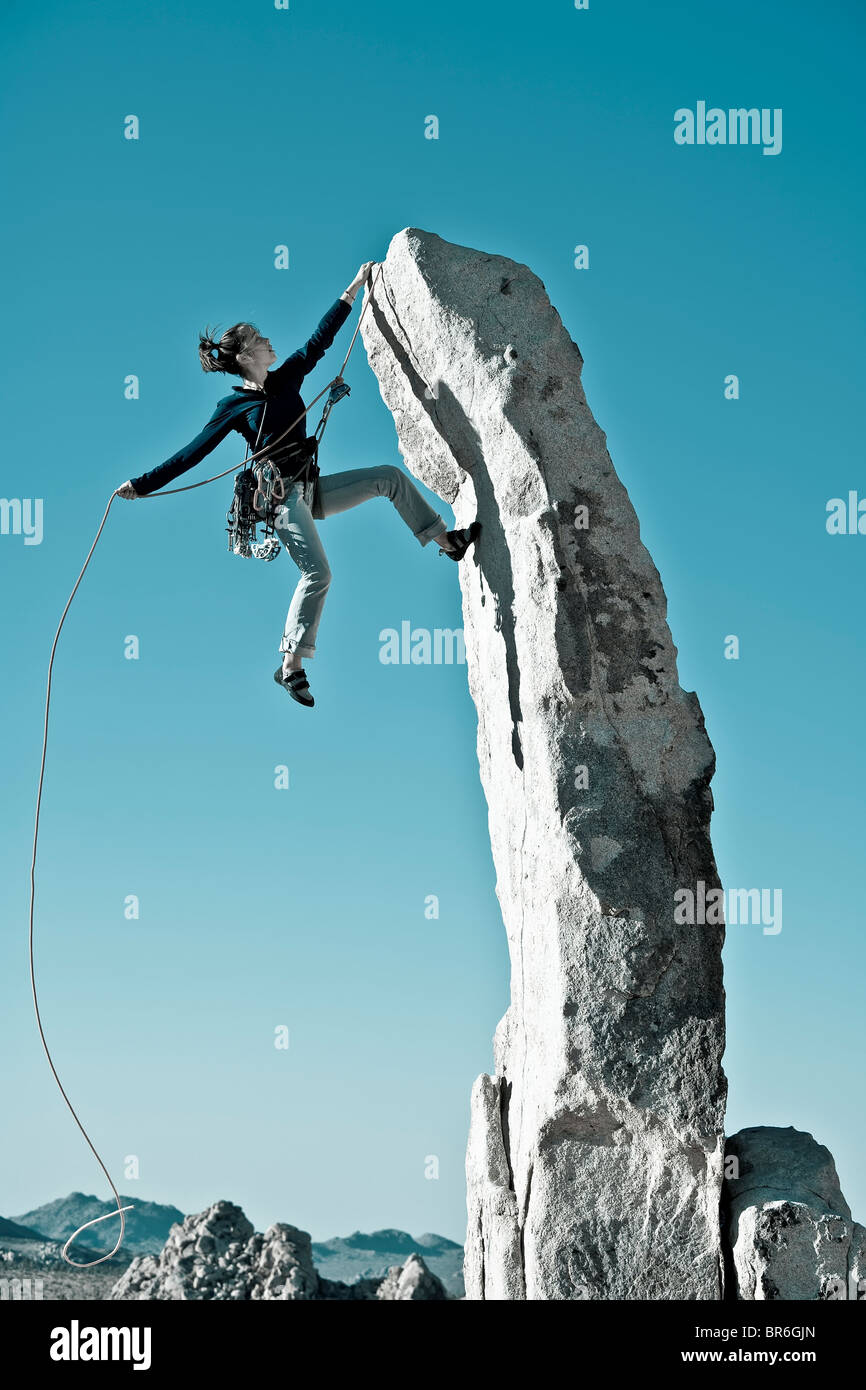 Climber in trouble dangling from her rope as she scales a rock pinnacle in the remote Mojave Desert of California. Stock Photo