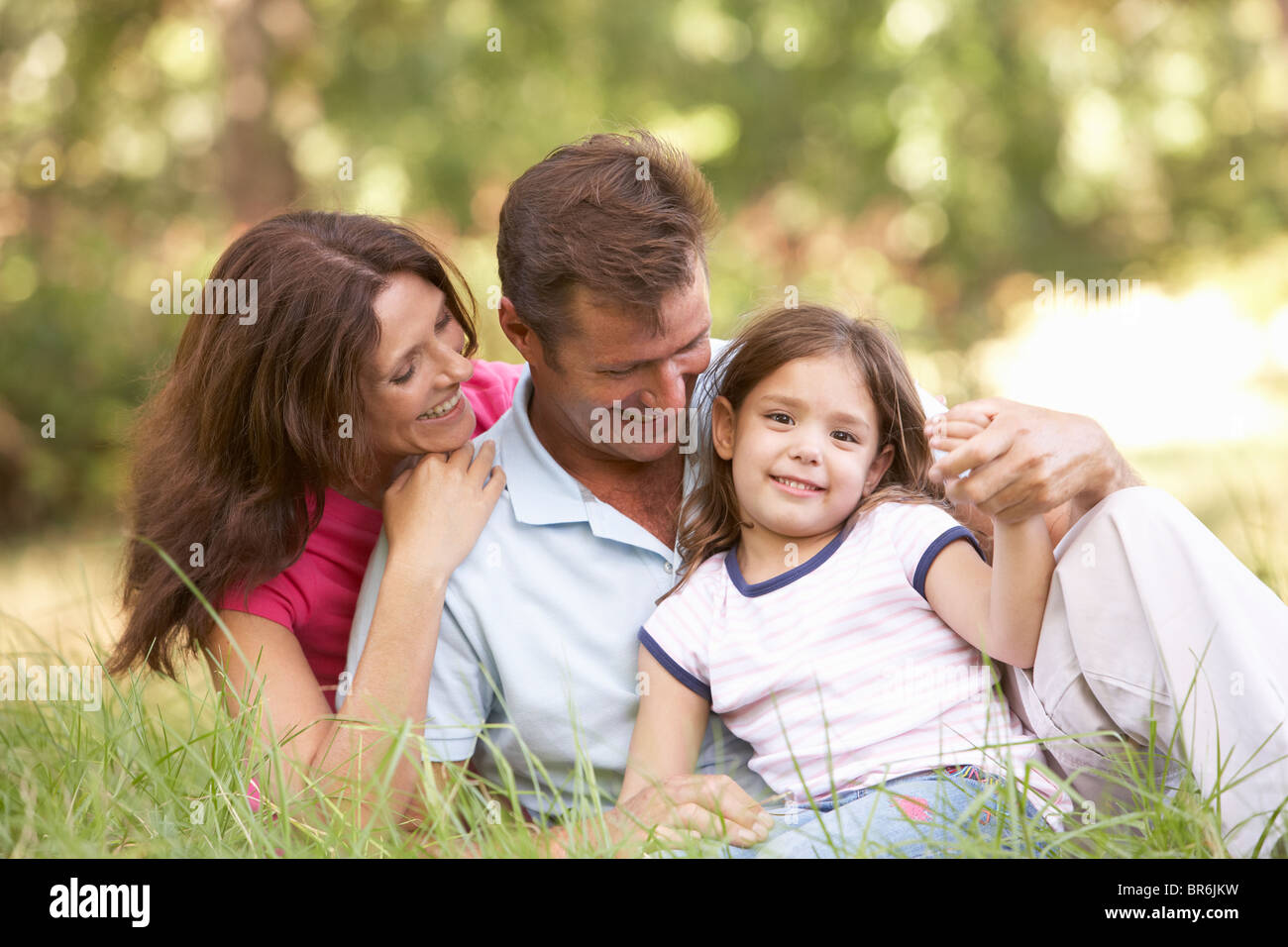 Family Sitting In Long Grass In Park Stock Photo
