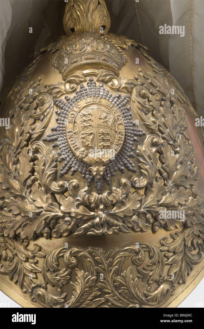 A fine helmet for officers of the Honourable Corps of Gentlemen at Arms., Gilded tombac skull fitted with superimposed, gilt mountings of oak leaves and foliage in relief. In the centre of the front side a vertically oval English coat of arms circumscribed with the motto of the Most Noble Order of the Garter 'Honi soit qui mal y pense' and set on a silver diamond-cut star. Leather-backed chinscales on embossed lion's head buttons and decorated with oak leaves (four scales missing), lion's paw clasp. White swan feather plume on a flamed socket. The peaks lined w, Stock Photo