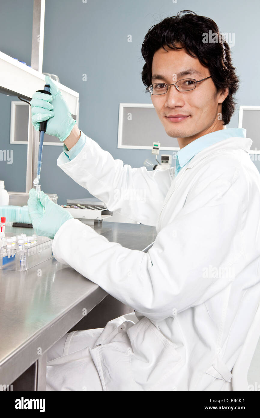 A lab technician using a pipette to put a sample into a vial, looking