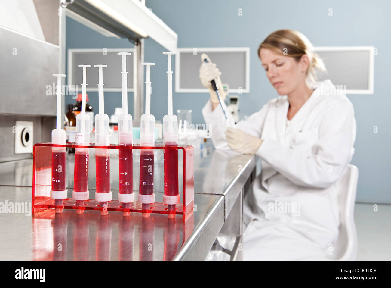 A row of vials holding blood and a lab technician working in background