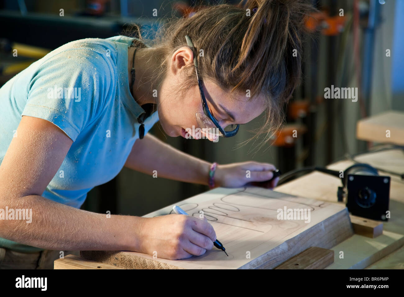 Young female apprentice sanding a cabinet part in a woodshop. Stock Photo