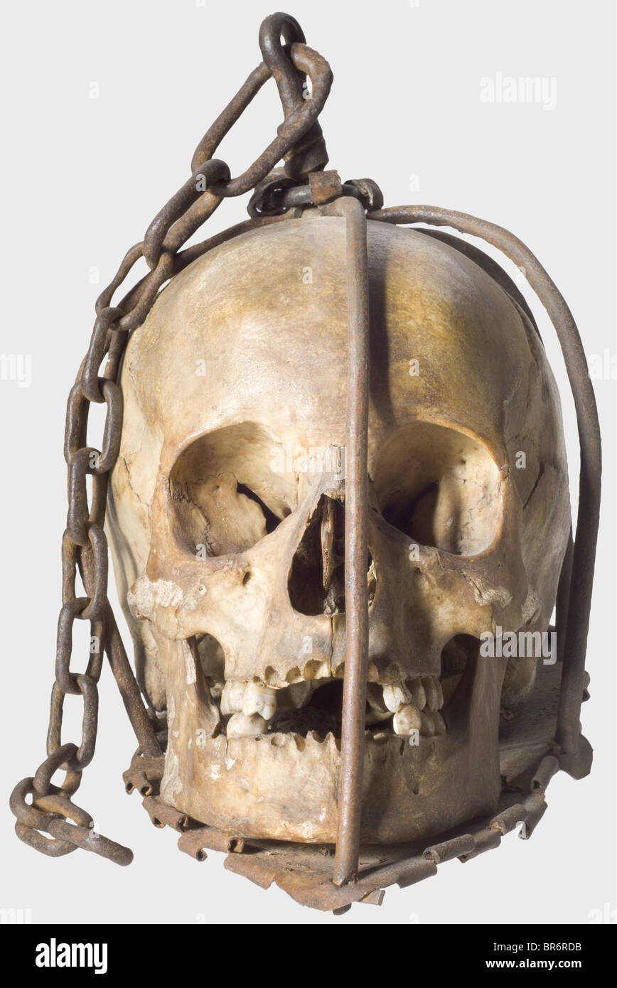 A skull of an execution victim, Germany, 16th/17th century. Wrought iron cage consisting of six bars (one replaced), cotter-pinned to an iron baseplate. The bars joined at the crown with an attached suspension chain. Within the cage a female(?) skull showing clear sign of age. Height 22 cm. Devices like this were hung at execution places to deter delinquents. historic, historical,, people, 17th century, 16th century, instrument of torture, torture device, instruments of torture, torture devices, object, objects, stills, clipping, clippings, cut out, cut-out, cu, Stock Photo