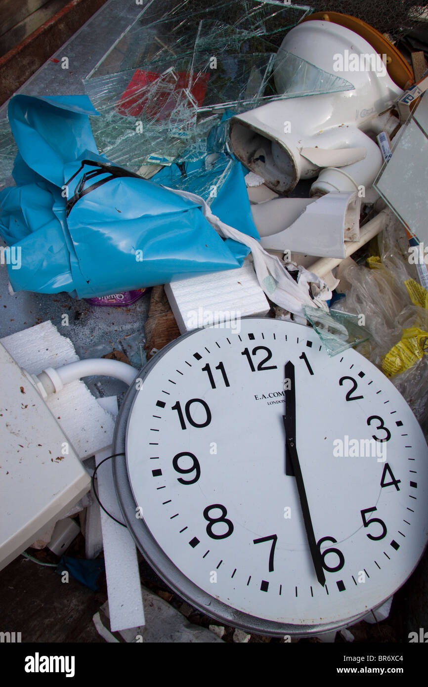 Large clock face at 12:31 in a skip/dumpster of rubbish including a toilet and cistern Stock Photo