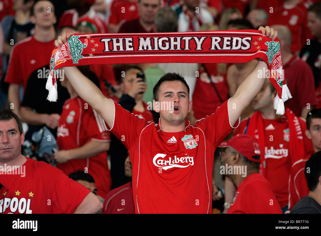 A Liverpool football fan holds up a scarf in the stands during a match Stock Photo