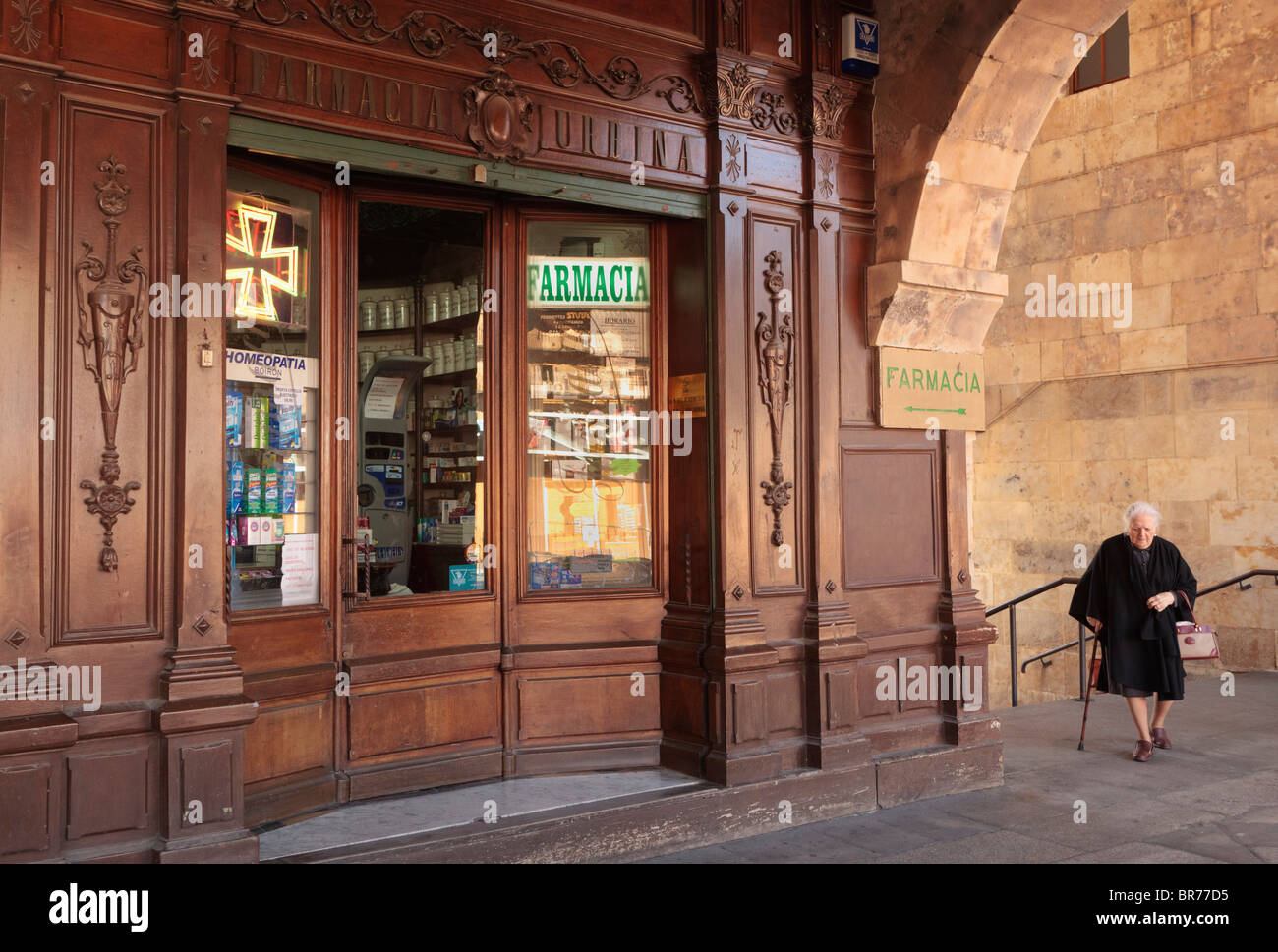 Woman Dressed In Black Walking By Wooden Fronted Chemist Shop In The Plaza Mayor; Salamanca, Salamanca Province, Spain Stock Photo