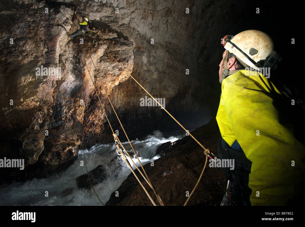 A cave explorer watches on as another de tackles the ropes in a cave in New Britain Stock Photo