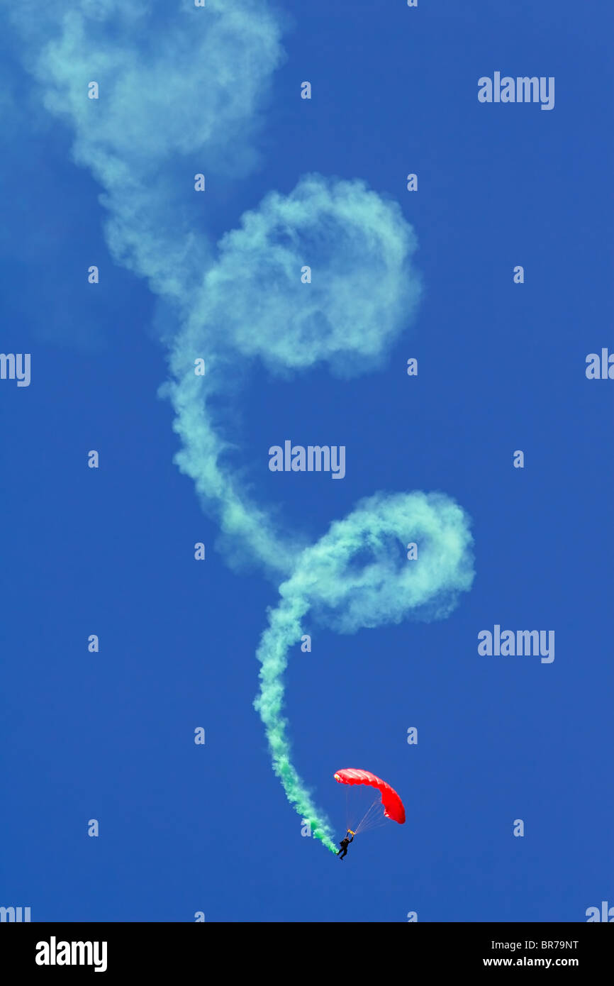 A parachutist performing a looped descent with smoke trail during an aerobatic show Stock Photo