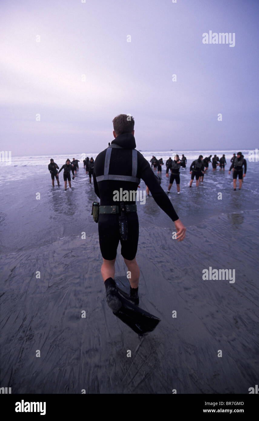 Man in a wetsuit and fins running into the ocean in San Diego