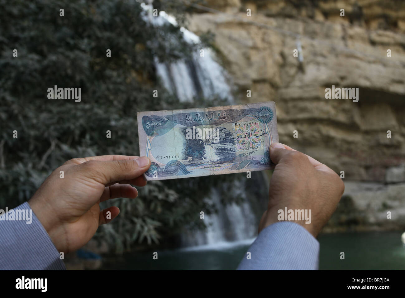A man holds a 5,000 Iraqi dinar at the waterfall of Geli Ali Beg which is pictured in the banknote Kurdistan Northern Iraq Stock Photo
