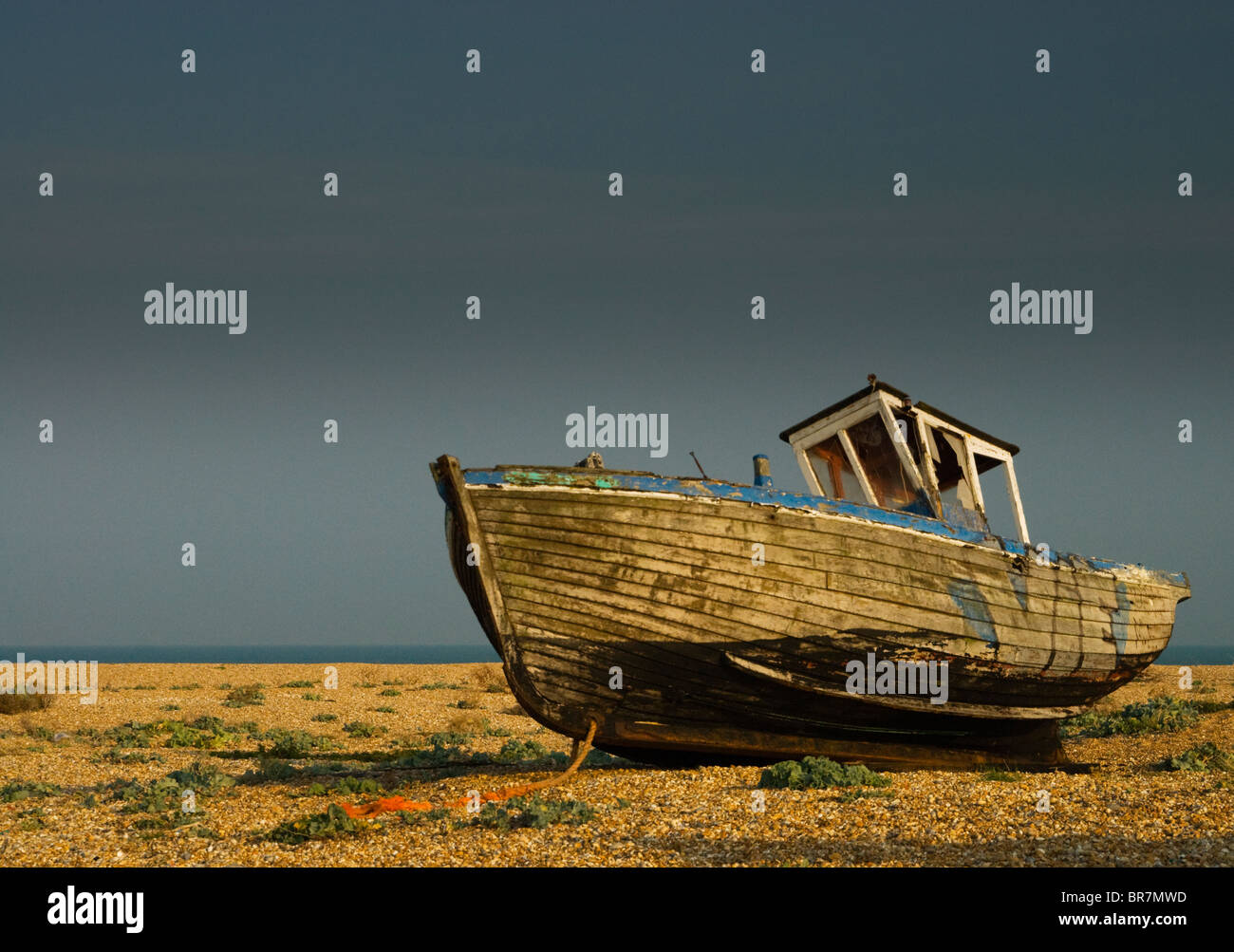 Old abandoned boat on Dungeness beach, against a grey stormy sky. Stock Photo