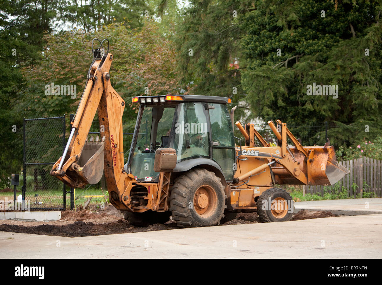 A yellow Case tractor with a backhoe and front loader in a pit. Stock Photo