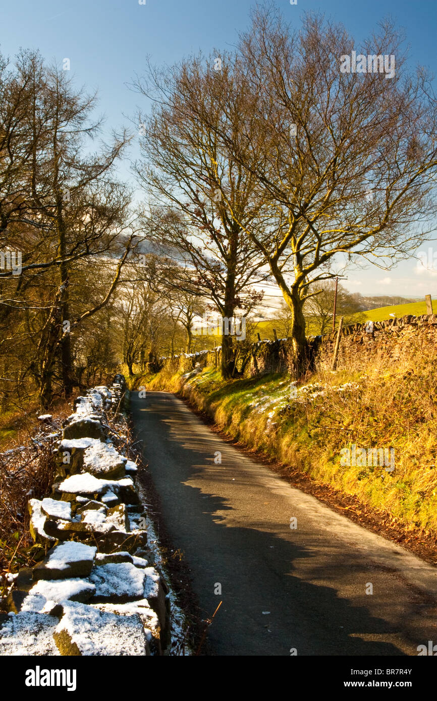 winter scene of dry stone wall covered in snow and lane leading to snow laden hills Stock Photo