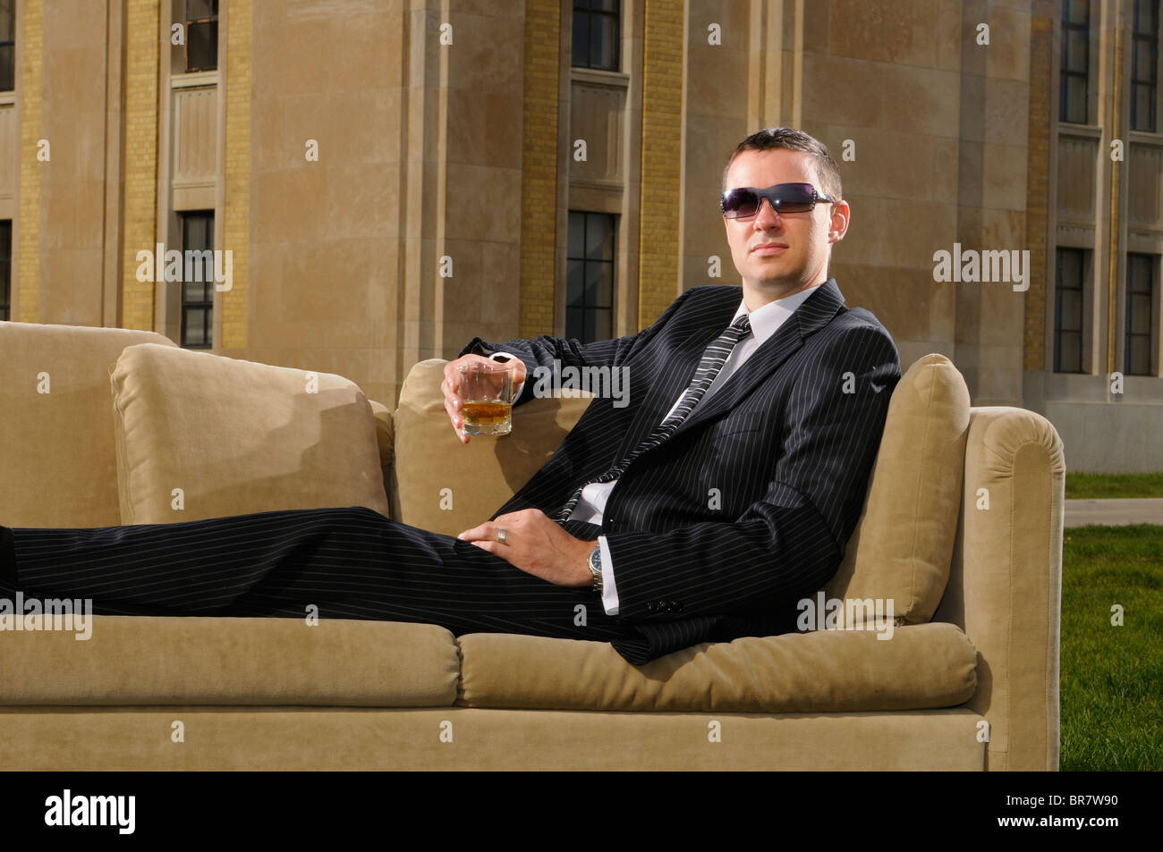 Wealthy young professional in suit lying on a couch with a drink at an Art Deco mansion RC Harris water treatment plant Toronto Stock Photo