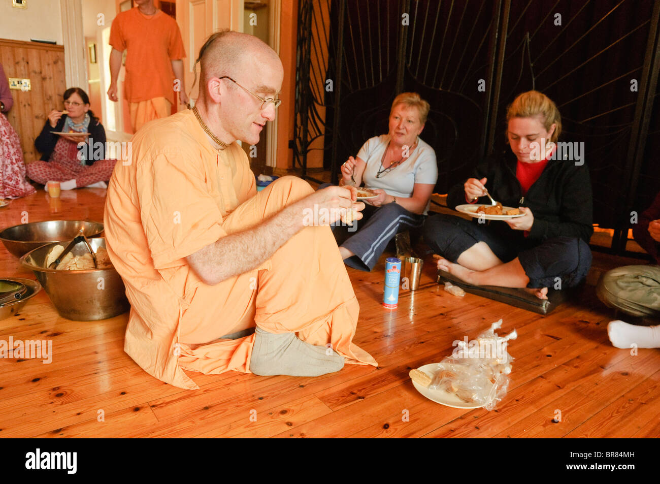 Hare Krishna devotee wearing saffron robes explains his religion to guests in a Hare Krishna temple room Stock Photo