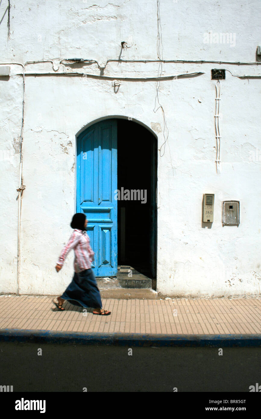 10th September 2009; A woman walks passed an open blue door in Essaouira, Morocco. Picture by David Pillinger. Stock Photo
