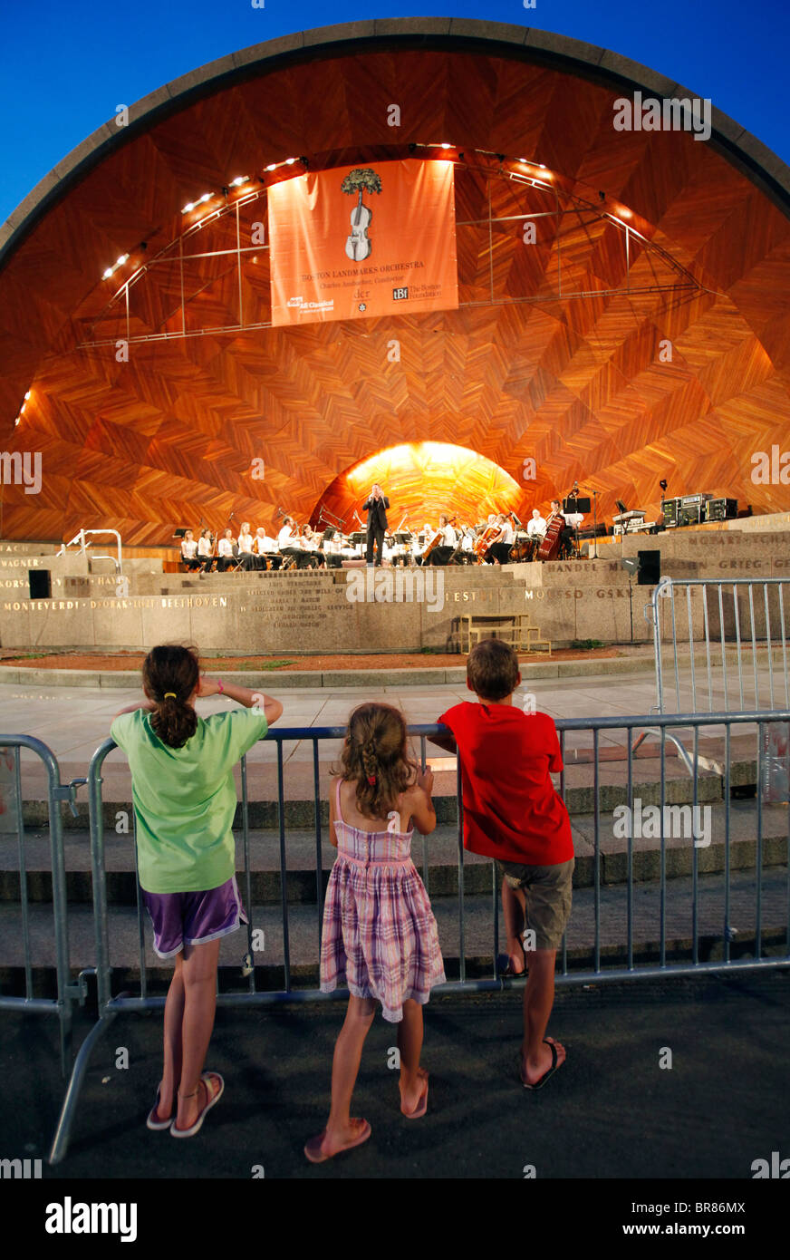 Three children watch a performance of the Boston Landmarks Orchestra at the Hatch Shell in Boston Massachusetts Stock Photo