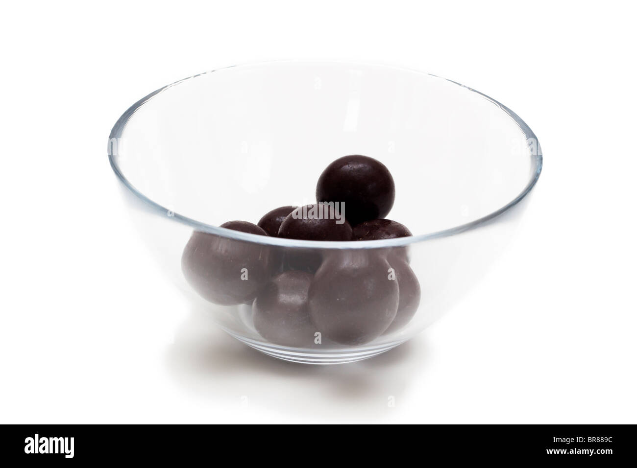 Chocolate covered macadamia nuts in a half empty glass dish Stock Photo