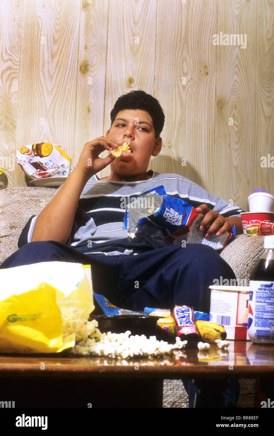 obese heavy overweight teen boy male Hispanic junk food overeat eat food excessive sit couch exercise TV health Stock Photo