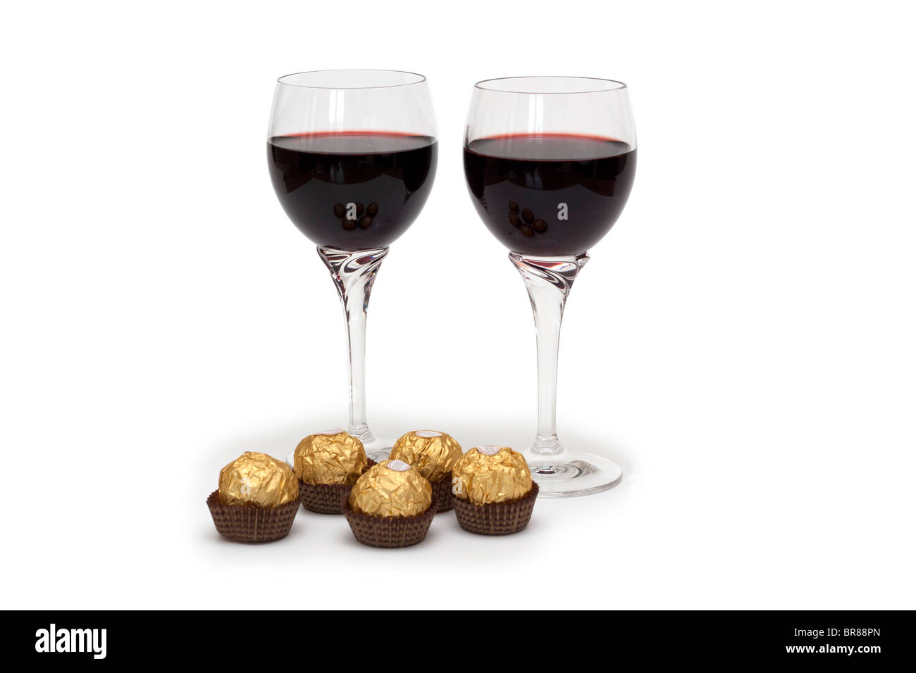 Two glasses of red wine with foil wrapped chocolates Stock Photo
