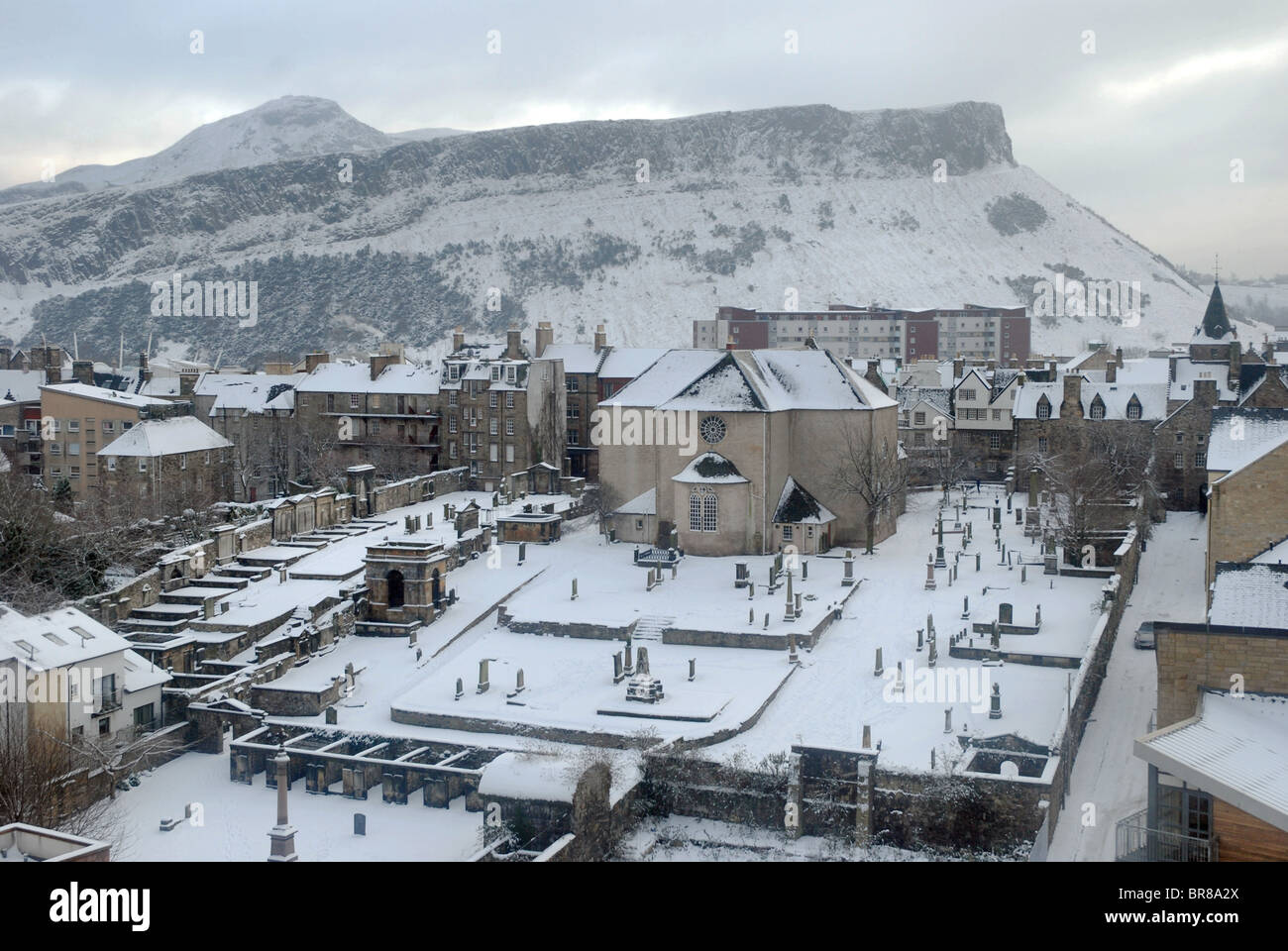 A wintry urban landscape, looking over the 17th century Canongate Kirk towards Salisbury Crags and Arthur's Seat in Edinburgh. Stock Photo
