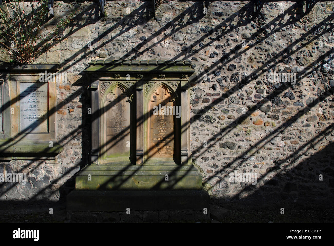 The sun casts shadows of ironwork onto memorials on a wall in South Leith Parish churchyard, Edinburgh, Scotland. Stock Photo