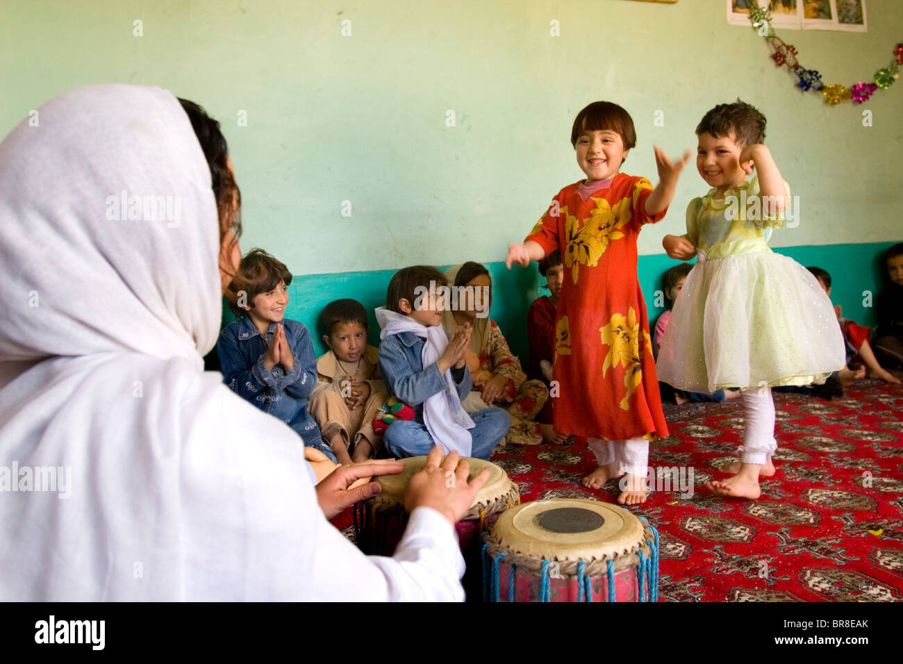 Children dance at a Kabul preschool while their teacher drums a rhythm. Stock Photo